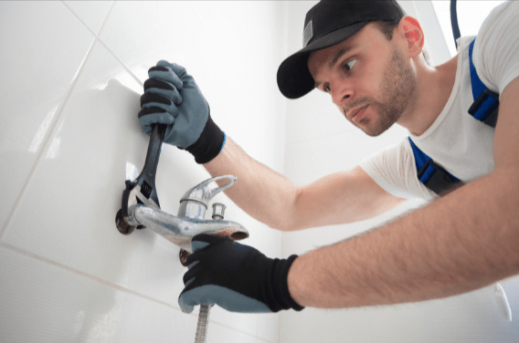 A plumber fixing a faucet with a wrench.