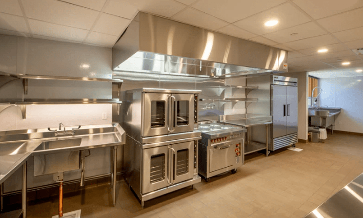 A commercial kitchen with oven racks, and large compartment sinks with faucets.