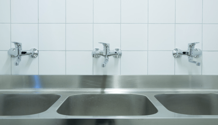 A row of commercial sinks and faucets of stainless steel.