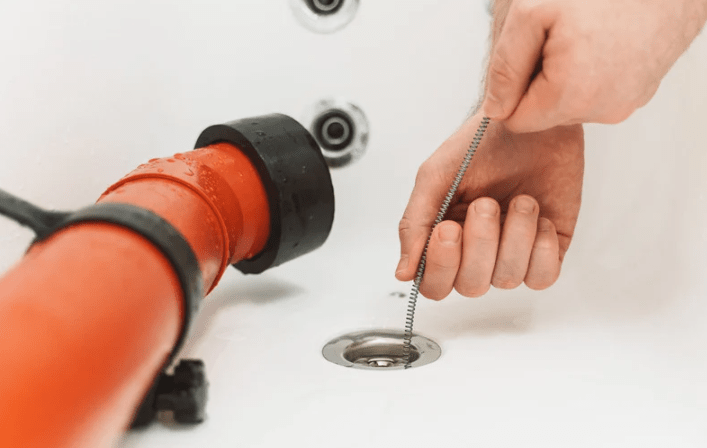 Hands threading a pipe cleaner brush on a wire stick inside a drain.