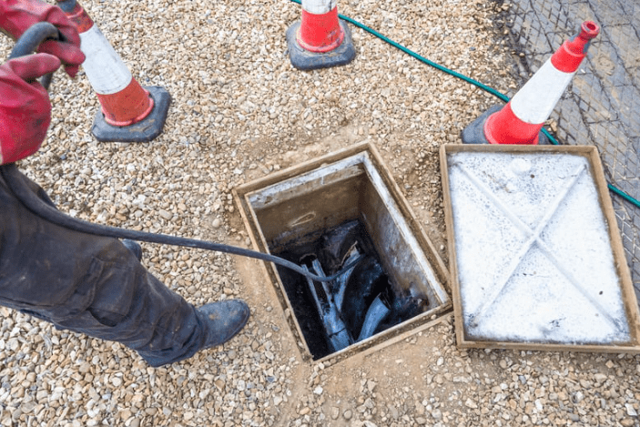 A plumber is using a cable inside a drain in the ground to clear a blockage.